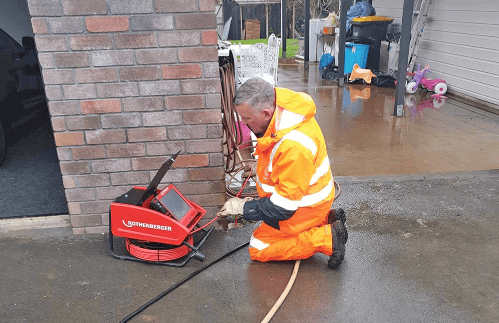 Man in orange protective gear working a cctv drain inspection machine