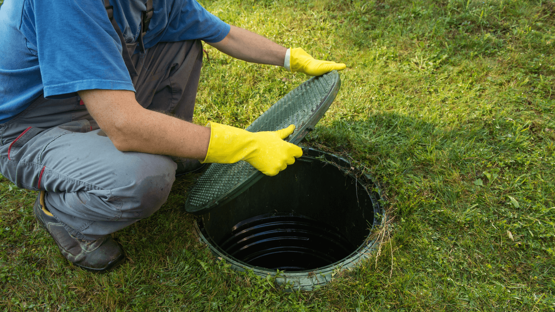 Man picking up septic tank cover with yellow gloves on